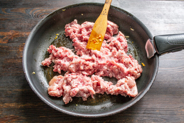 Searing Homemade Ground Meat for the Funchoza Sauce Raw homemade ground meat being placed into a hot, oiled frying pan to start the sauce.