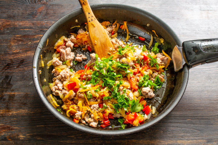 Combining Meat, Vegetables, and Herbs for the Funchoza Sauce Cooked ground meat, sautéed vegetables, and fresh herbs being mixed together in a pan.