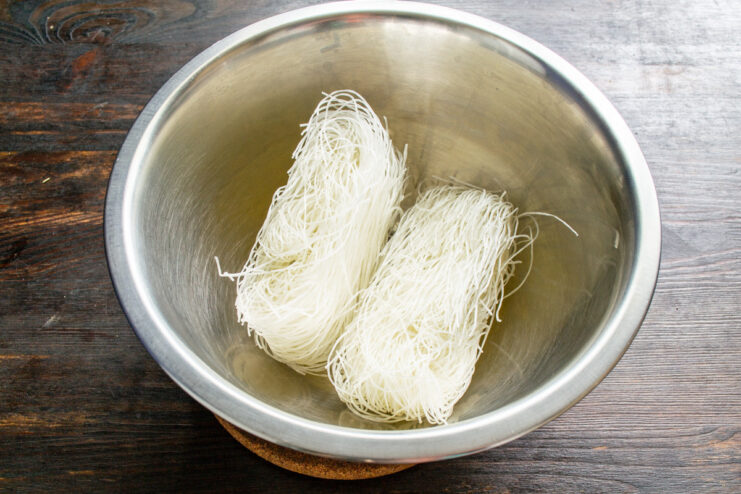 How to Properly Rehydrate Funchoza (Glass Noodles) Dry funchoza noodles in a white bowl with boiling water being poured over them.