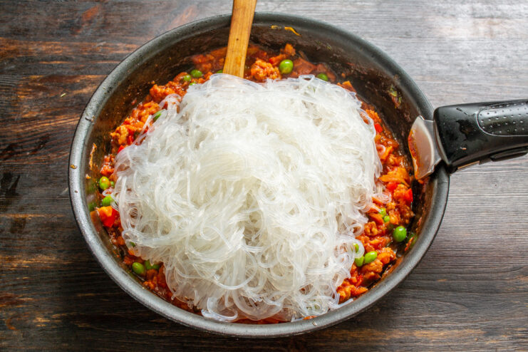 Tossing the Cooked Funchoza with the Savory Meat Sauce Cooked, translucent funchoza noodles being added to the pan with the meat sauce.