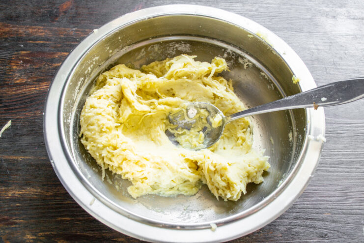 A spoon mixing the potato, flour, and buttermilk dough in a bowl.