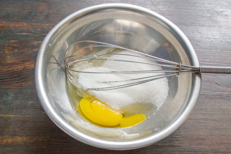 Step 1: Whisking an egg with sugar in a glass bowl. A glass bowl with an egg and sugar being mixed with a whisk.