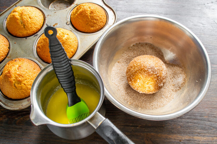 Step 9: Brushing the warm buns with melted butter. A freshly baked bun being brushed with melted butter using a silicone pastry brush.