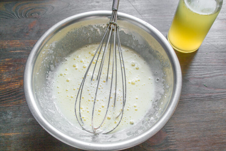 Step 3: Adding apple cider to the egg and sugar mixture. Pouring apple cider into the whisked egg and sugar mixture in a glass bowl.