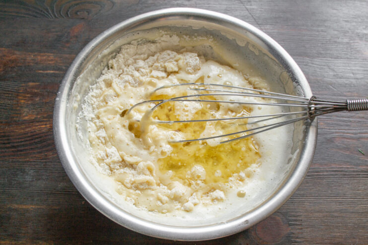 Step 5: Adding oil to the bun batter. Pouring oil from a small glass jug into the batter.