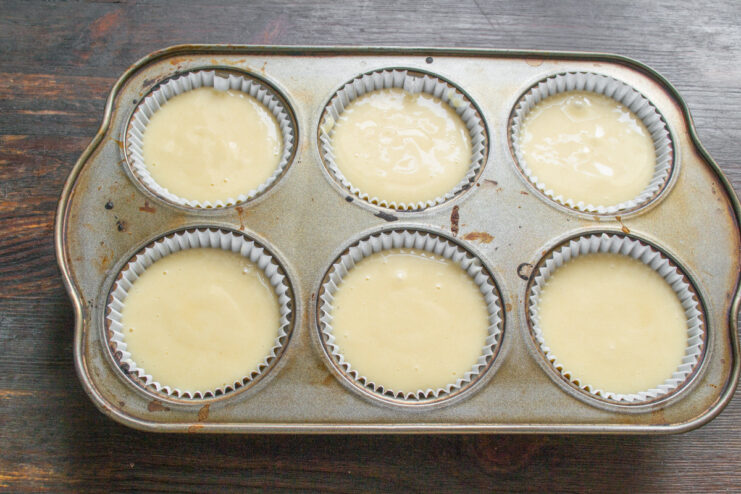 Step 7: Filling the muffin tin with batter. A muffin tin with paper liners being filled with batter for the cinnamon buns.