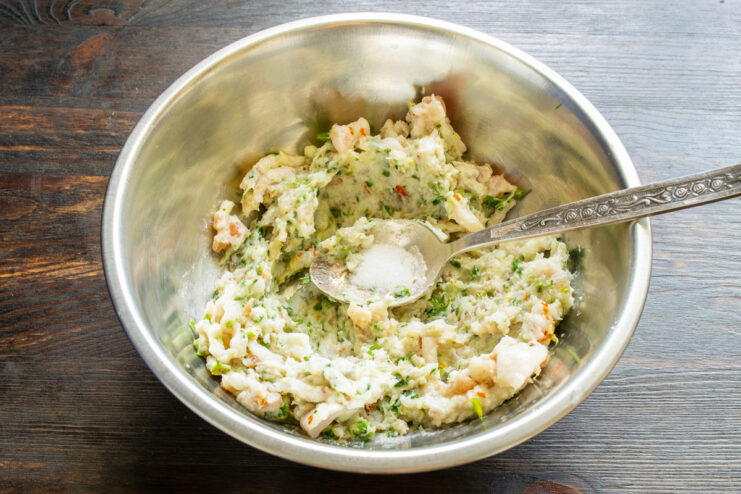Creating the perfect texture: Grinding all ingredients together. Ingredients like salo, garlic, and herbs being fed into a meat grinder.