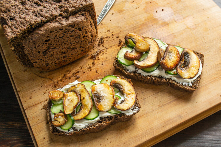 Topping the Sandwich with Pan-Fried Mushrooms Golden-brown fried mushroom slices being placed on top of the cucumber layer.