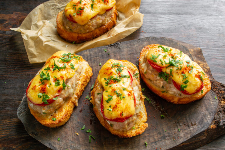 Garnishing Hot Baked Sandwiches Before Serving Hot baked open-faced sandwiches on a plate, garnished with fresh parsley and paprika.