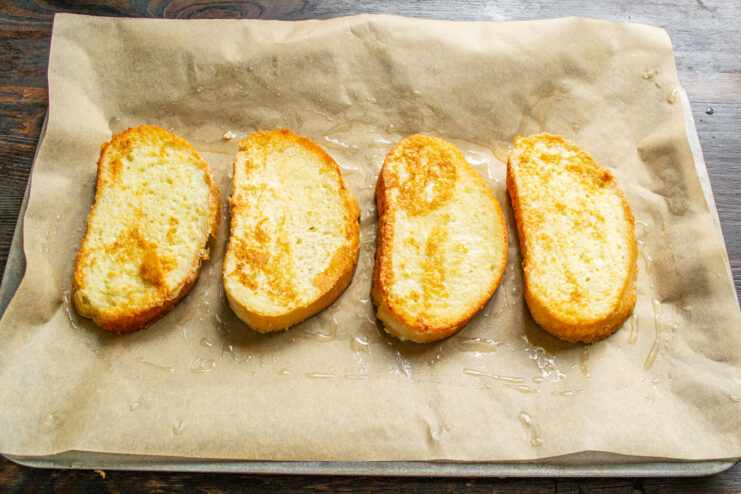 Arranging Fried Bread on a Baking Sheet Four slices of golden-fried bread arranged on a parchment-lined baking sheet.