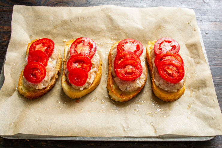 Topping the Meat Patties with Tomato Slices Thin slices of fresh tomato being placed on top of the meat patties.