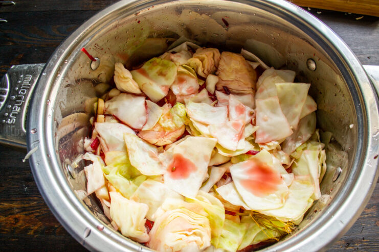 Combining Everything: Pouring the Cooled Brine Over the Cabbage Mixture Cooled pickling brine being poured over the cabbage, beets, and apples in a pot.