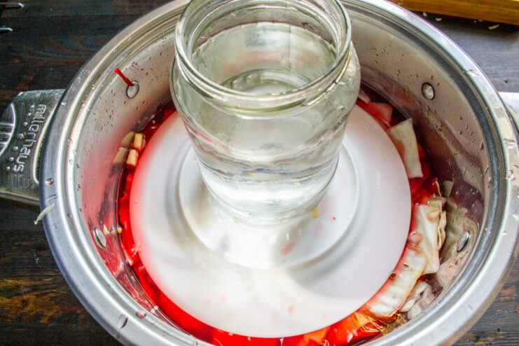 How to Keep Vegetables Submerged in Brine: Using a Plate as a Weight A plate is placed on top of the vegetables in the pot to keep them submerged.