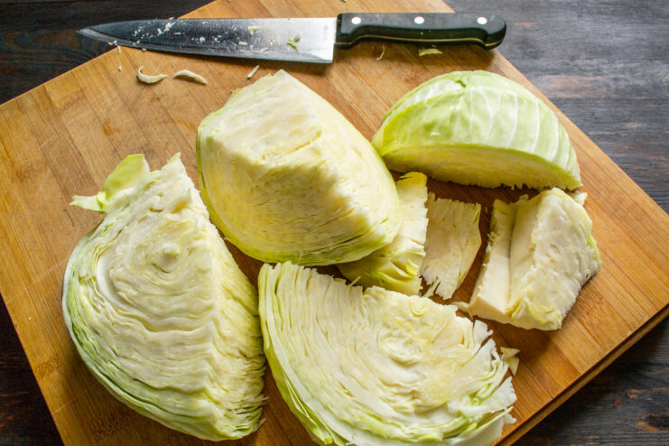 How to Prepare Cabbage for Pickling: Cut the Head in Half A head of white cabbage being cut in half on a wooden cutting board.