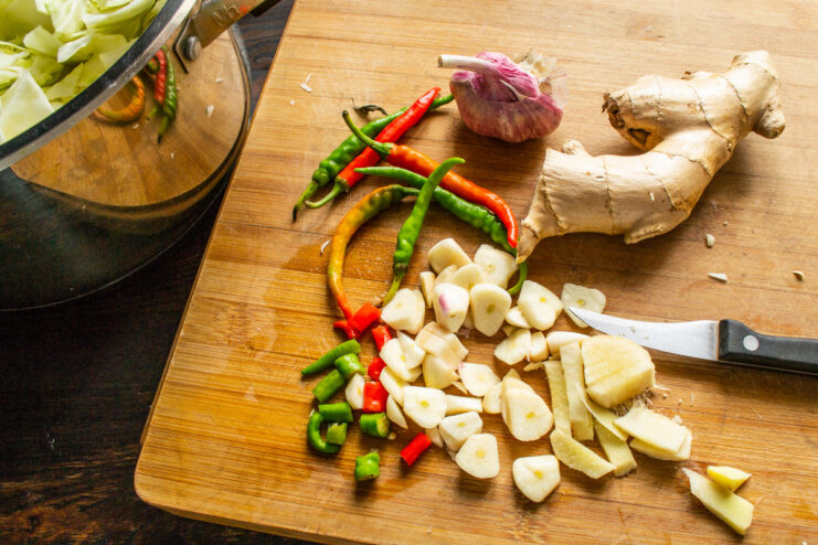 Adding Flavor: Thinly Sliced Garlic and Ginger for Pickled Cabbage Fresh ginger root and garlic cloves being thinly sliced on a cutting board.