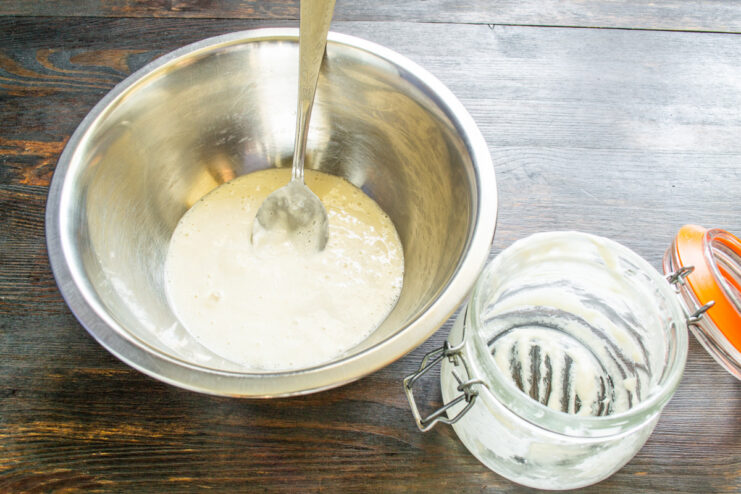 Active sourdough starter being transferred from a jar to a deep mixing bowl.
