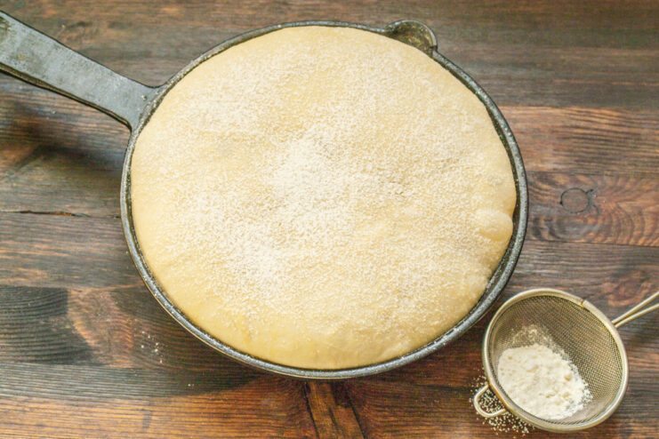 Shaped loaf of sourdough bread proofing in a cast-iron skillet.