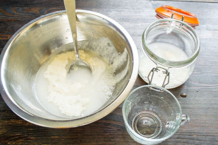 Pouring 70 grams of water into the bowl containing the sourdough starter.