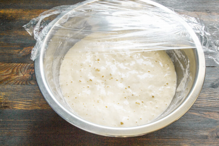 A mixing bowl with leaven covered tightly with plastic wrap to ferment.