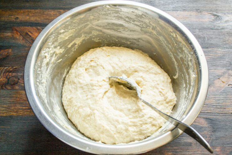 Hands kneading the wet and sticky sourdough bread dough in a bowl.