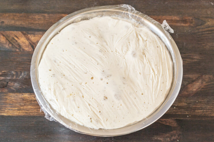 Sourdough dough rising in a bowl, covered with plastic wrap.