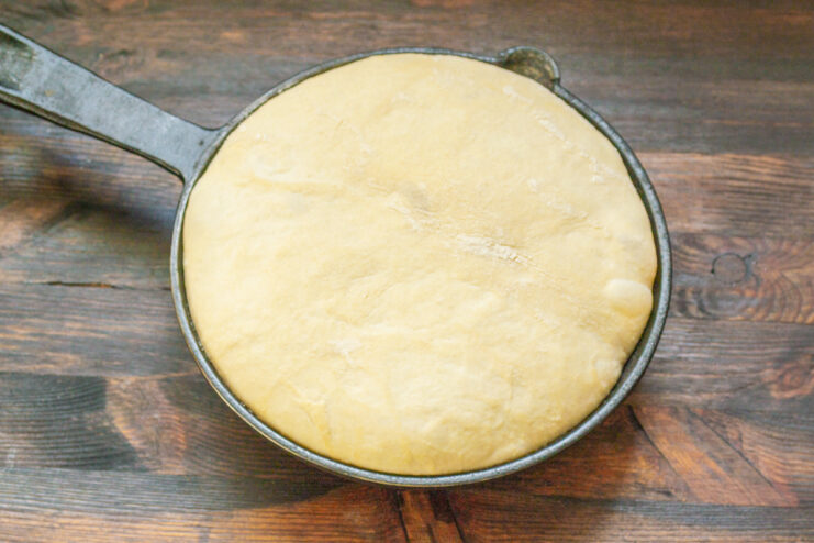 Shaping the risen dough into a round loaf before placing it in a cast-iron skillet.