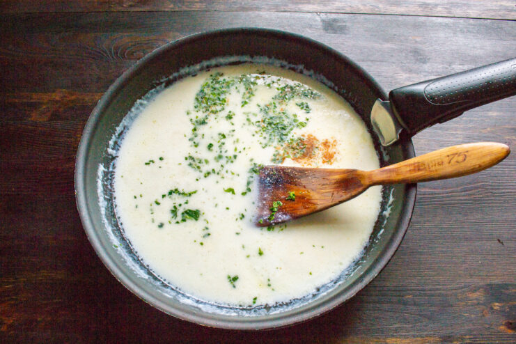 Bringing the creamy milk sauce to a boil A creamy white milk sauce simmering in a skillet.