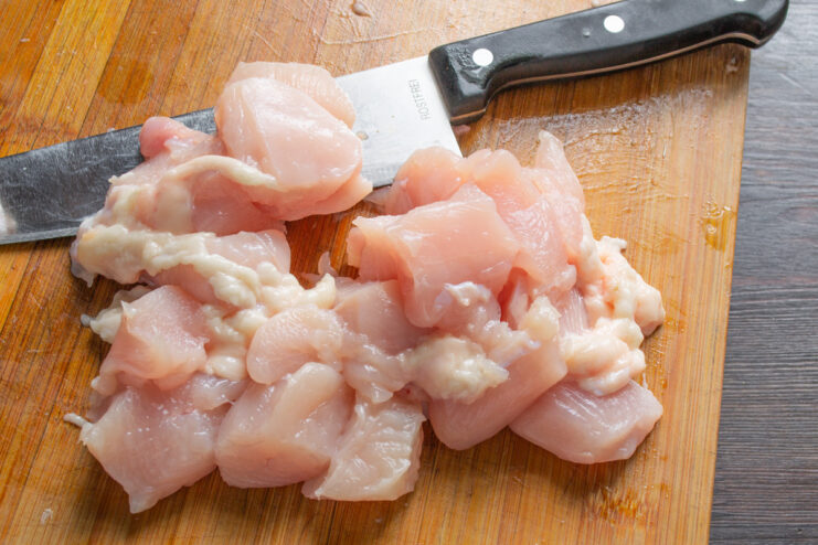 Preparing Chicken Breast for Patties A hand holding a knife, cutting a fresh chicken breast fillet away from the bone.