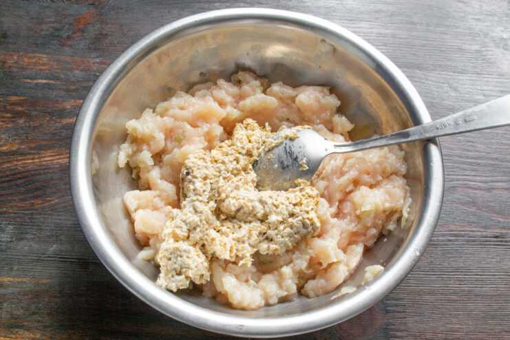 Combining Oats with Ground Chicken Soaked oatmeal being added to a bowl of ground chicken mixture.