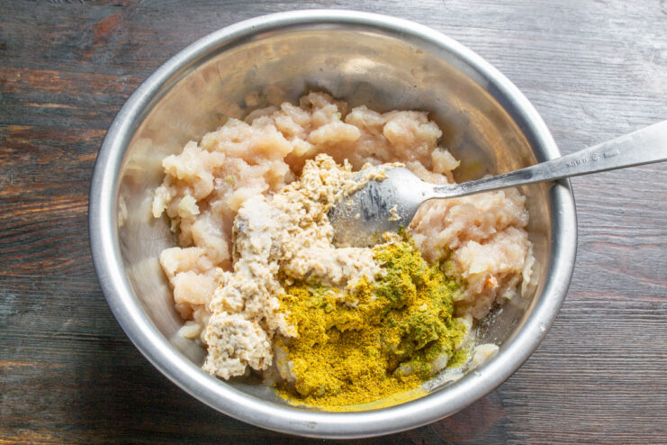 Seasoning the Chicken Patty Mixture A hand sprinkling dried herbs and spices into the ground chicken mixture.