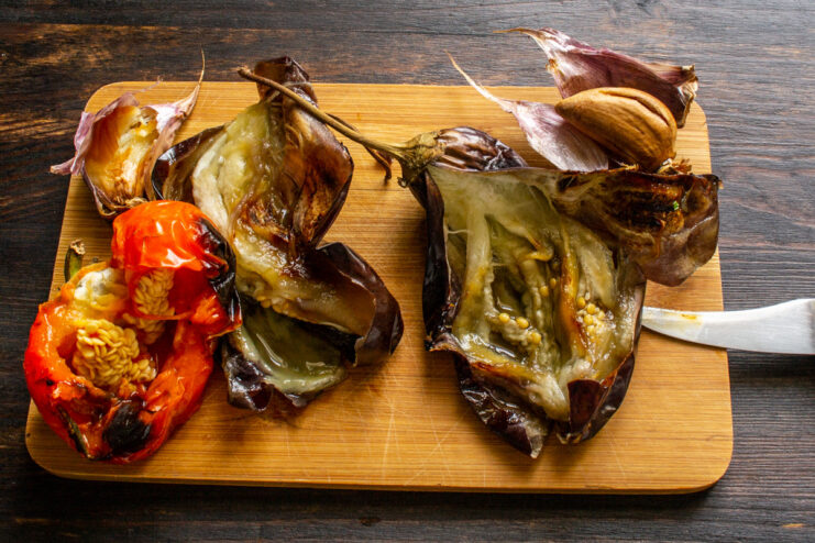 Cooling the Roasted Vegetables Before Peeling Roasted and slightly charred eggplant, bell pepper, and garlic cooling down after being taken out of the oven.
