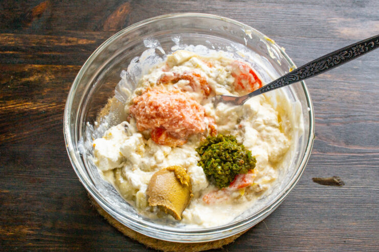 Seasoning the Dip with Spicy Condiments Adding horseradish, adjika, and mustard to the vegetable and cheese mixture in a bowl to create a spicy dip.