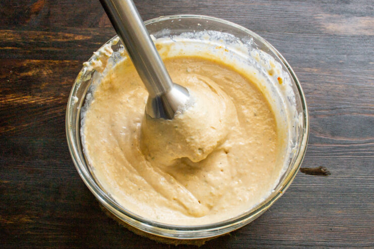 Blending the Dip Until Smooth Using an immersion blender to mix the roasted vegetable dip in a bowl until it reaches a smooth, creamy consistency.
