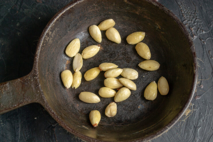 Toasting Peeled Almonds to Enhance Flavor Peeled almonds being toasted in a dry frying pan until lightly golden.