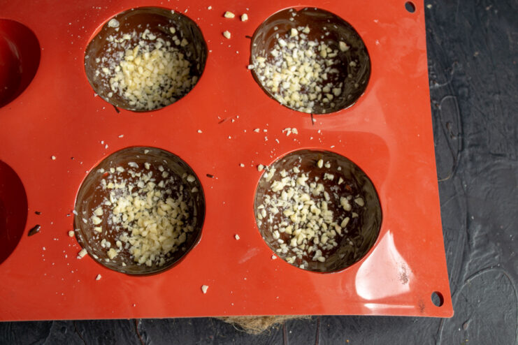 Adding a Layer of Almond Crumbs to the Chocolate Shell Melted chocolate in a silicone mold being sprinkled with finely chopped almonds.