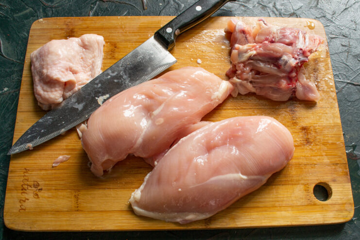Prepping the Chicken Breast for Sardelki A hand removing the skin from a raw chicken breast on a cutting board.