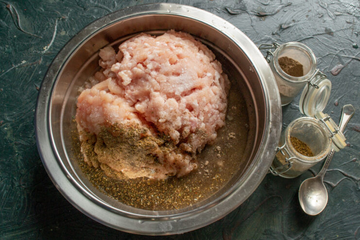 Seasoning the Sausage Meat with Spices A bowl of minced meat with ground allspice and crushed coriander being added.