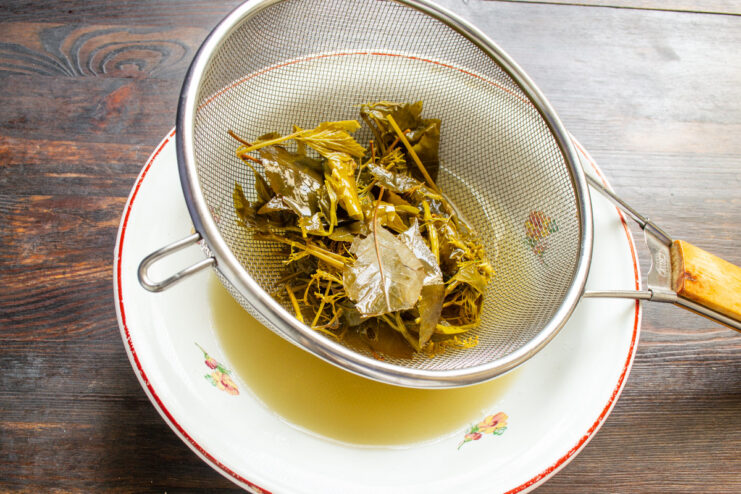 Straining Pickle Brine for a Smooth Mustard Base Straining cloudy pickle brine through a fine-mesh sieve into a glass bowl.