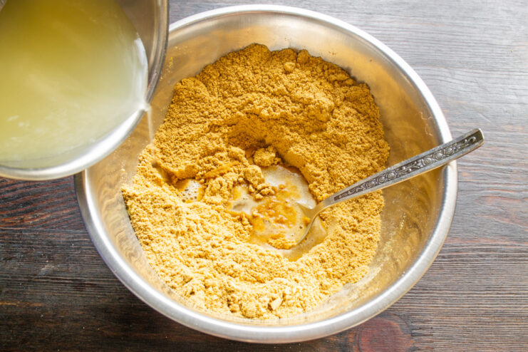 Combining Hot Brine with Mustard Powder Pouring hot pickle brine from a saucepan into a bowl with mustard powder and spices.