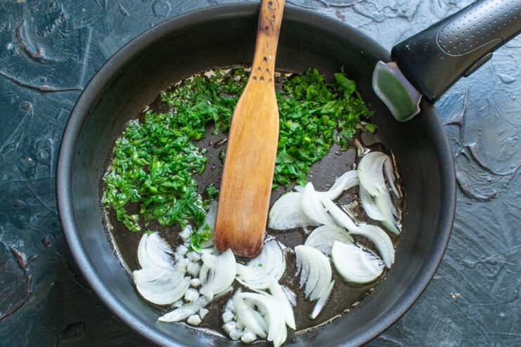 Sautéing Onions and Parsley for the Frittata Base Chopped onion and parsley being sautéed in melted butter in a black skillet.