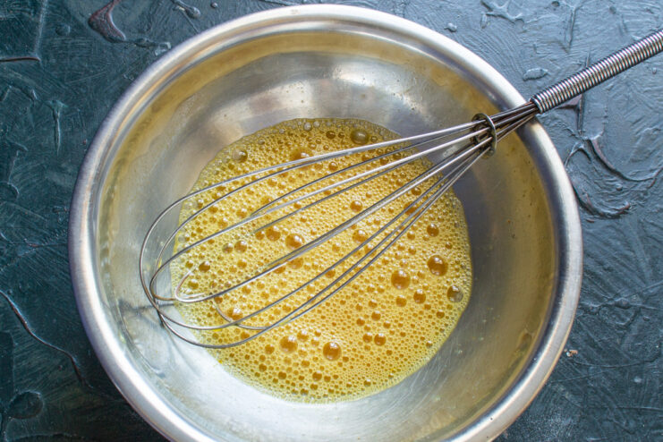 Whisking Eggs Until Smooth for a Fluffy Frittata Whisking eggs in a glass bowl until they are a uniform yellow liquid.