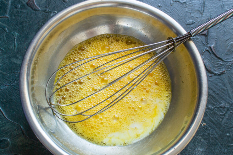 Adding Milk to the Egg Mixture for a Creamier Texture Pouring milk from a measuring cup into the whisked eggs in a bowl.