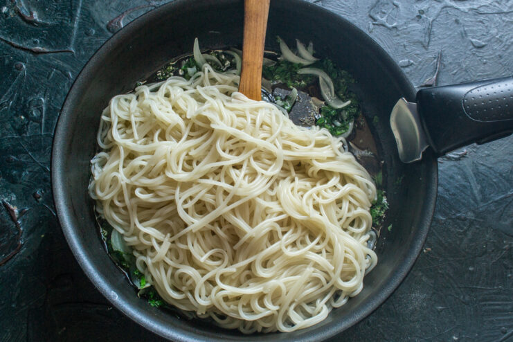 Combining Cooked Vermicelli with Sautéed Vegetables Cooked vermicelli being added to the skillet with sautéed onions and parsley.
