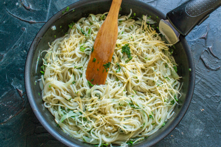 Topping the Vermicelli with Grated Cheese Before Adding Eggs A layer of cooked vermicelli in a skillet being sprinkled with grated cheese.