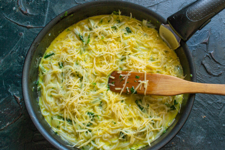 Ensuring an Even Layer for a Perfectly Cooked Frittata Shaking a skillet to evenly distribute the egg and vermicelli mixture.