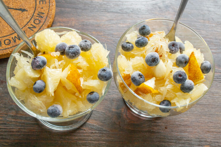 Adding fresh blueberries for a burst of color and flavor Fresh blueberries being sprinkled over the pomelo fruit salad in a glass bowl.