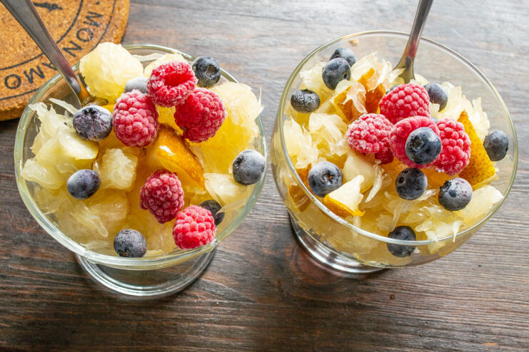 Final touches: garnishing with raspberries before serving A finished pomelo fruit salad in a glass bowl, garnished with raspberries and blueberries.