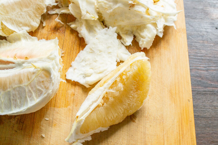 Step-by-step guide to segmenting a pomelo Close-up of pomelo segments with the white pith being removed.