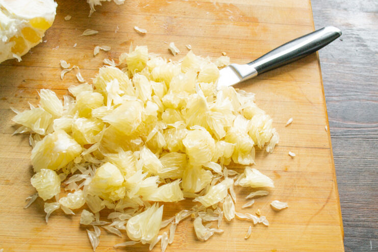 Chopping pomelo segments into bite-sized pieces Peeled pomelo segments being chopped into smaller pieces on a cutting board.