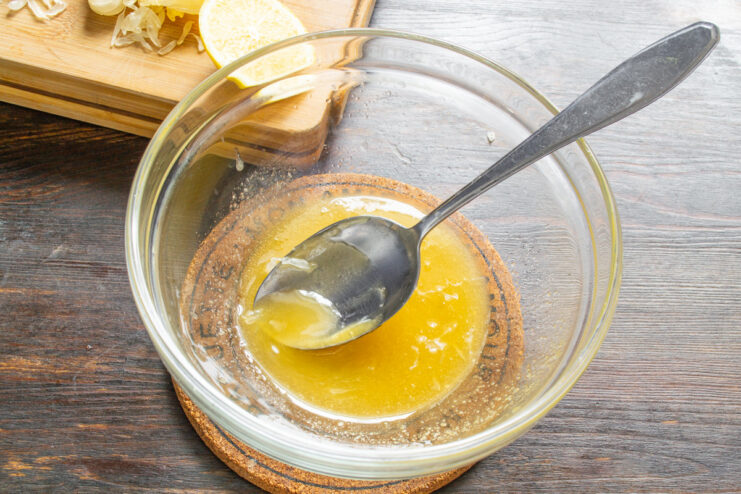 The perfect consistency for a honey-lemon fruit salad sauce A spoon mixing honey and lemon juice in a white bowl to create a smooth dressing.